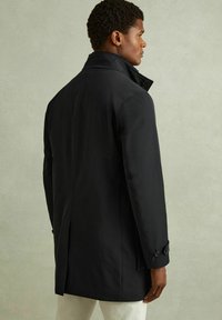 Must be veekindel must jope, millel on kõrge krae, stiilne disain, nööbitavad varrukad ja taga vent, valmistatud siledast kangast.