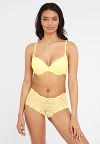 Yellow lace bra with a smooth padded design and adjustable straps, paired with matching lace hipster briefs featuring scalloped edges.