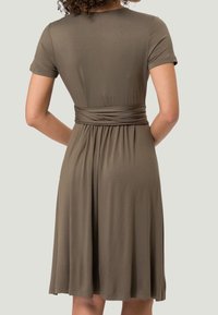 Robe à manches courtes, de couleur vert olive, fabriquée en matériau doux, avec une taille froncée et une jupe évasée. Design simple avec une texture lisse.