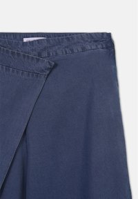 Primo piano di una gonna avvolgente blu navy con vita visibile e pannello frontale sovrapposto su uno sfondo bianco.