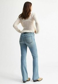 Suéter de punto beige claro con dobladillo acanalado, combinado con jeans acampanados azul claro. Ambas prendas tienen un corte relajado y texturas sutiles.