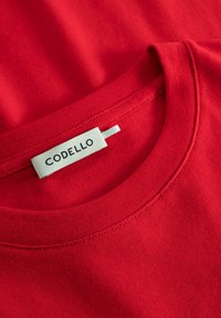 Rotes Baumwoll-T-Shirt mit Rundhalsausschnitt und einem sichtbaren Markenlabel mit der Aufschrift "CODELLO." Der Stoff hat eine glatte Textur und eine saubere Nahtverarbeitung.