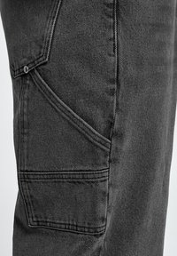 Pantalones cargo de mezclilla negra con un acabado texturizado, que presentan un bolsillo lateral y costuras decorativas a lo largo de las costuras.