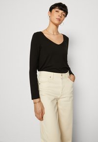 Black long-sleeve V-neck shirt paired with high-waisted, light beige wide-leg jeans; model poses with hands in pockets.