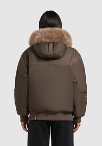 Brown puffer jacket with fur-trimmed hood, ribbed cuffs, and a relaxed fit. Features a smooth texture and subtle sheen.