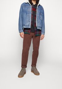 Jeansjacka med fårskinnskrage, rutigt skjorta under, grå T-shirt, bruna kordflöjlsbyxor och grå snörade ankelboots.