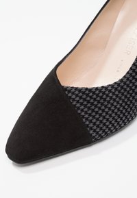 Zapato negro de punta afilada con textura de ante y diseño de tela de espiga. Forro interior suave con acentos de material en contraste.