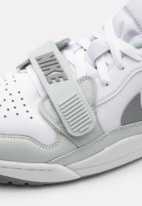 Basket Nike blanche et grise en gros plan montrant les lacets, la boîte à orteils perforée, les détails cousus et la bride ajustable marquée.