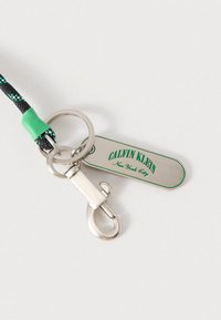 Μαύρο και πράσινο πλεγμένο μπρελόκ με ασημένιο εξάρτημα, διακοσμημένο με μεταλλική ταμπέλα με χαραγμένα τα λόγια "CALVIN KLEIN" και "New York City".