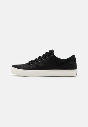Black sneaker with a breathable mesh upper, flat white rubber sole, and six eyelets. Features textured surface and a logo on the heel.
