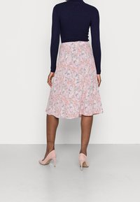 Blomstret nederdel i pink, hvid og grøn med en udskåret design. Kombineret med en tætsiddende marineblå top og lyserøde højhælede sko.