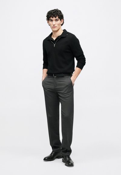 Black zip-up knit pullover, slim-fit gray dress pants, and black lace-up shoes. Plain and smooth textures with no prominent patterns.