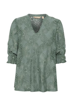 Vihreä pitsipaita, jossa on V-pääntie, lyhyet puffihihat, kukkakuosi ja teksturoitu kangas. Mukana kokoontuneet hihansuut ja löysä istuvuus.