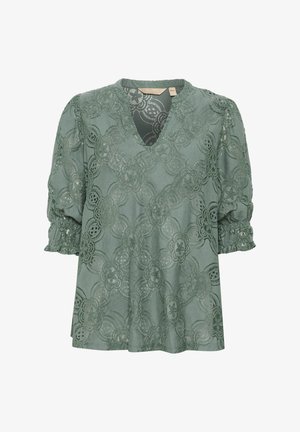 Vihreä pitsipaita, jossa on V-pääntie, lyhyet puffihihat, kukkakuosi ja teksturoitu kangas. Mukana kokoontuneet hihansuut ja löysä istuvuus.