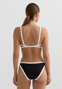 Czarny zestaw bikini z białymi akcentami. Regulowane paski i zapięcie na haczyk z tyłu. Gładka tkanina o klasycznym, minimalistycznym wzorze.