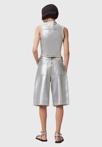 Silver metallic sleeveless vest and shorts with a smooth texture. Features visible stitching and pockets. Sandals complete the outfit.