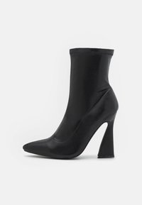 Bottines noires synthétiques avec un bout pointu, un talon haut effilé et une tige lisse et extensible qui monte au-dessus de la cheville.