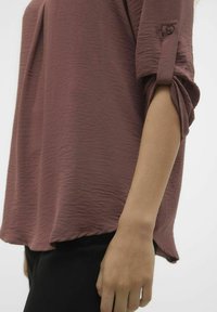 Blusa a maniche lunghe di color bordeaux con finitura strutturata, caratterizzata da maniche arrotolate e vestibilità rilassata. Realizzata in tessuto leggero.