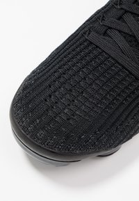 Svart stickad sportskor med en texturerad yta, rundad tå, snörning och en slät svart sula.