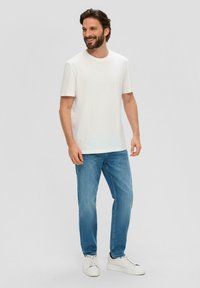 Witte katoenen T-shirt, korte mouwen, ronde halslijn, gecombineerd met lichtblauwe spijkerbroek en witte sneakers. Eenvoudige en casual outfit.