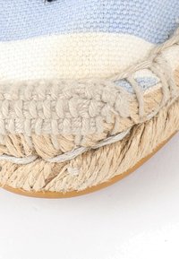 Gros plan de la semelle d’une espadrille tissée avec du jute tressé et des détails en fibres naturelles cousus sur le dessous en caoutchouc.