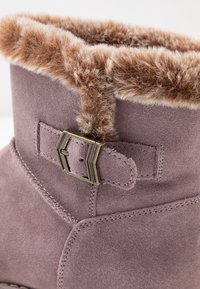 Fialová semišová bota s hnědým umělým kožichem na okraji, kovovou přezkou a podrobným prošíváním podél švů.