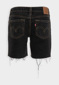 Mustat farkkushortsit, joissa on repaleinen helma, ommellut takataskut, joissa on erottuva kaareva muotoilu, sekä ruskea nahkainen tuotetunniste vyötäröllä.