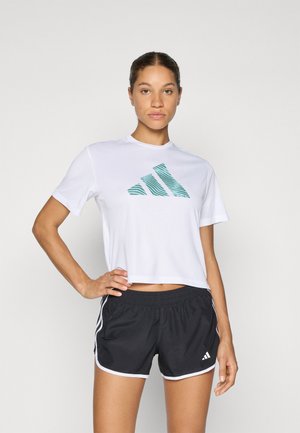 Witte cropped t-shirt met een teal gestreepte Adidas-logo, gecombineerd met zwarte sportshorts met witte zijaccenten en een elastische tailleband.