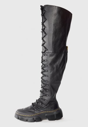 Botte noire haute en cuir avec lacets, semelle épaisse et couture jaune, s'étendant au-dessus du genou.