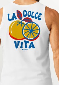 Weißes Tanktop mit buntem Grafikdesign eines Orangen- und Zitronenmotivs mit roten Blättern. Der Text lautet "LA DOLCE VITA" in blauer Schrift, das Markenlogo darunter.