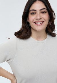 Lichtgrijze sweatshirt met korte mouwen en subtiele bloemrijke borduursels. Gladde textuur en eenvoudige, ronde halslijn, met een relaxte pasvorm.