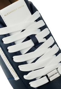 Sneaker in pelle blu navy con lacci bianchi, caratterizzato da un logo dorato sulla linguetta e un accento argento sul lato. Texture liscia.