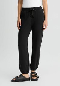 Pantalons de jogging noirs en matériau doux avec une taille élastique et un cordon de serrage réglable. Comprend des panneaux en mesh sur les côtés et des ourlets resserrés.