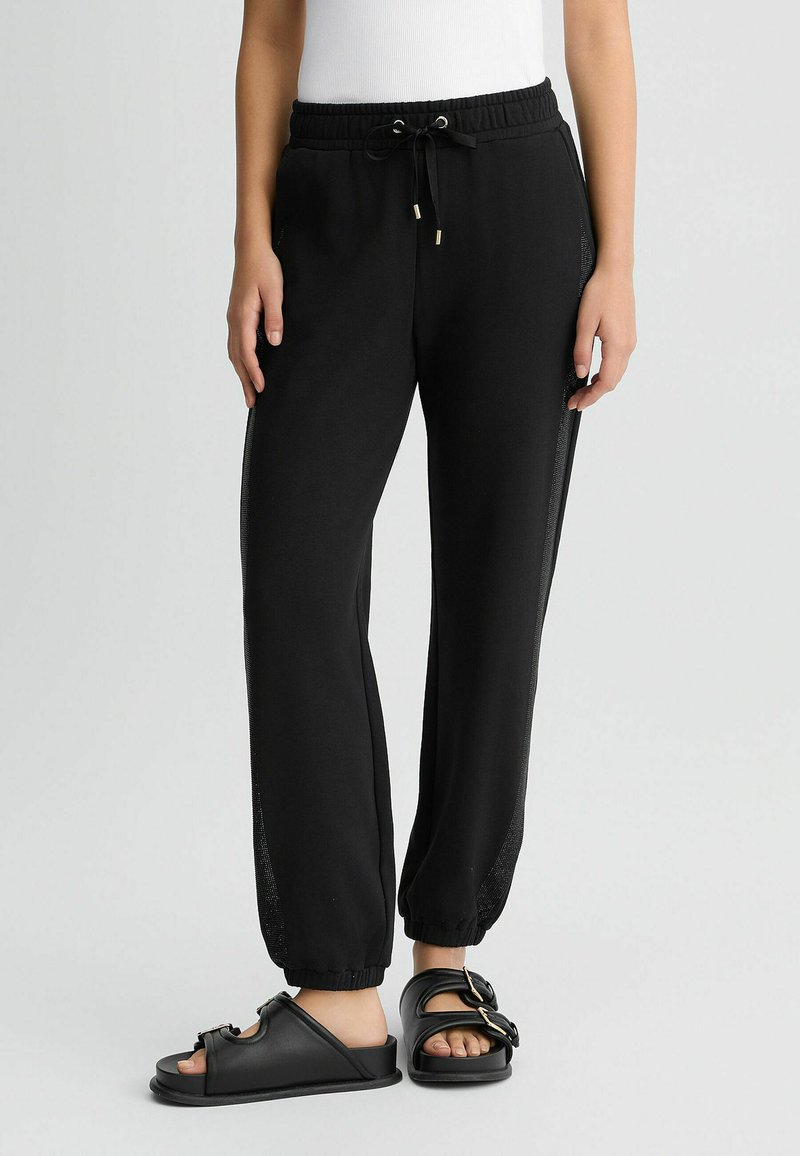 Pantalons de jogging noirs en matériau doux avec une taille élastique et un cordon de serrage réglable. Comprend des panneaux en mesh sur les côtés et des ourlets resserrés.