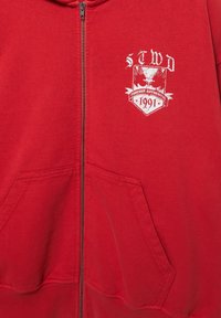 Rød lynlås-hoodie med forlommer og hvid grafik på brystet med teksten "STWD Forever Authentic 1991" og ørne-design.