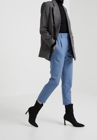 Blazer à carreaux noir et blanc, col roulé noir ajusté, pantalon sur mesure bleu clair, et bottines à talons noirs.