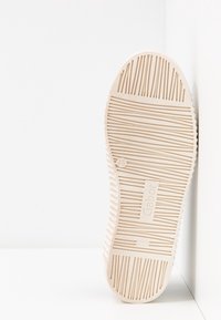 Hnědá gumová podrážka boty s texturovanými, liniovými vzory a obdélníkovým logem. Obsahuje mírně zakřivený okraj a vertikální drážky pro lepší přilnavost.