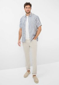 Short-sleeve striped shirt in blue and white linen, paired with light beige trousers and beige slip-on shoes, showcasing a relaxed fit.