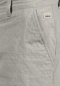 Shorts gris clair en tissu texturé, ornés d'un motif de petits losanges, avec une étiquette de marque visible et des poches.