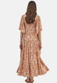 Vestido maxi en marrón claro con un patrón de conchas. Tejido fluido, mangas acampanadas y diseño con volantes. La vista trasera muestra un escote fruncido y un detalle texturizado.