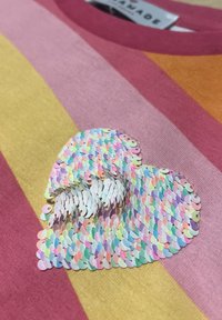 Gestreiftes T-Shirt mit einem mehrfarbigen, schimmernden Pailletten-Herzdessin. Die Farben umfassen Pink, Gelb und Orange mit einer sanften Textur.