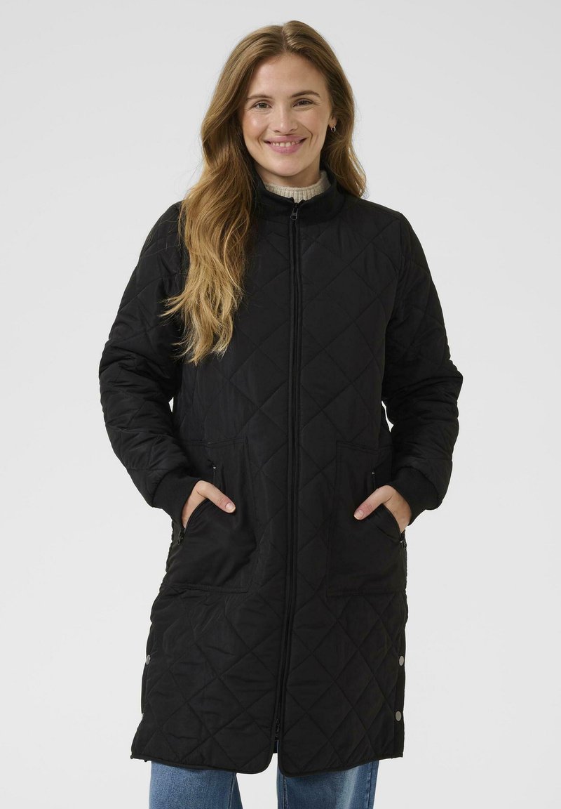 Manteau long noir matelassé avec col montant, fermeture éclair, poches latérales et poignets côtelés. Il présente un motif en losanges et une coupe décontractée.