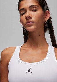 Wit sporttop met een ronde hals, voorzien van een zwart Jordan-logo in het midden. Glad materiaal met een aansluitend ontwerp.