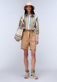 Camicia a righe verde e multicolore, pantaloni corti beige, cappello a secchiello beige e sneakers con accenti in gel. Materiale in cotone, vestibilità comoda, design casual.