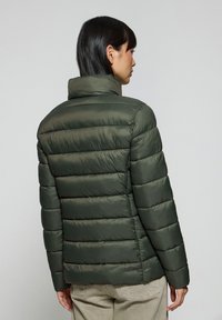 Olivgrön puffjacka med hög krage, horisontell quiltad textur och slätt tyg. Har en figurnära silhuett och diskreta sömmar.