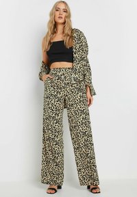 Leopardmönstrad set bestående av en svart cropped topp och vida byxor med en beige bakgrund, prydd med svarta fläckar och sidofickor.