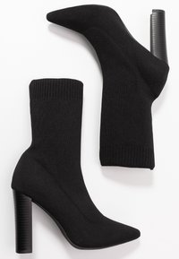 Czarne dzianinowe botki sięgające kostki z szpiczastym noskiem i prążkowanym mankietem, z teksturowanym czarnym obcasem. Gładkie wykończenie i elastyczny materiał.