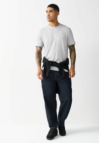 Grå bomulds t-shirt med korte ærmer, parret med mørk denim jeans, sort sweater knyttet om livet og sorte sko.