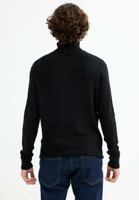 Pulóver negro de manga larga con cuello alto, textura de punto suave y puños ajustados; combinado con jeans de mezclilla azules con bolsillos traseros.