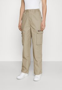 Beige cargobroek met elastische tailleband, meerdere zakken en een lichte glans. Gecombineerd met witte sneakers en een aansluitend wit topje.